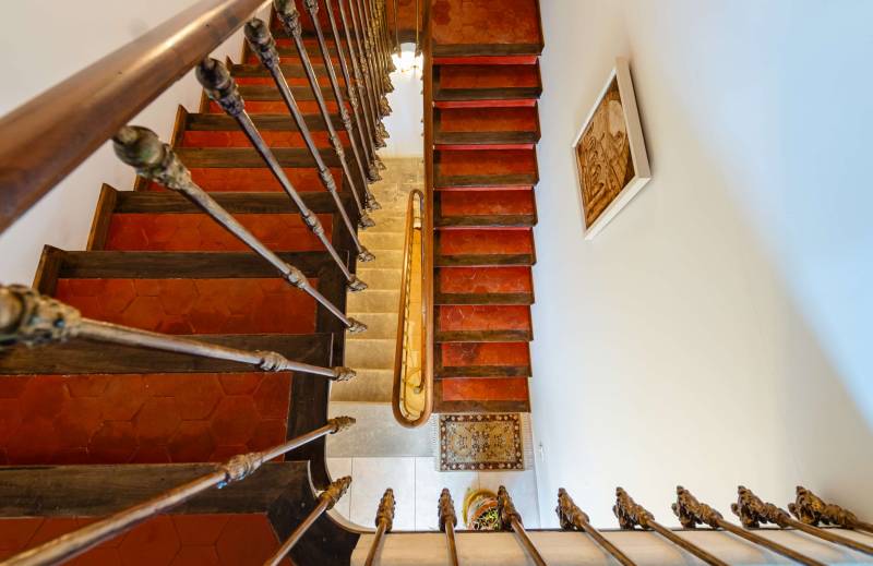 Perspective view of the grand, historic staircase with authentic red-tile steps and wrought-iron rail.