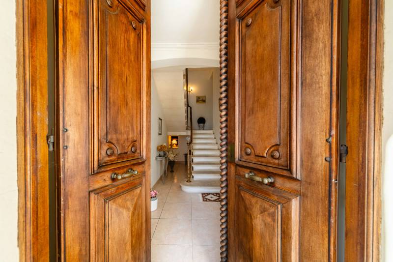 Grand double wooden entrance doors, revealing the elegant hall and historic staircase.